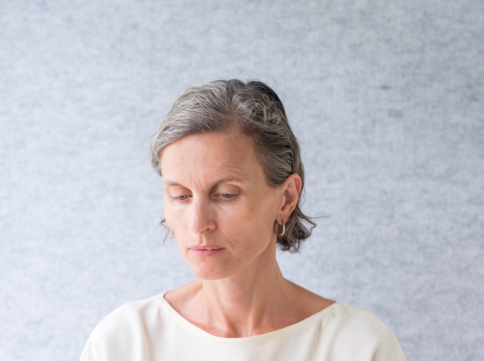 Middle aged woman looking down against grey background