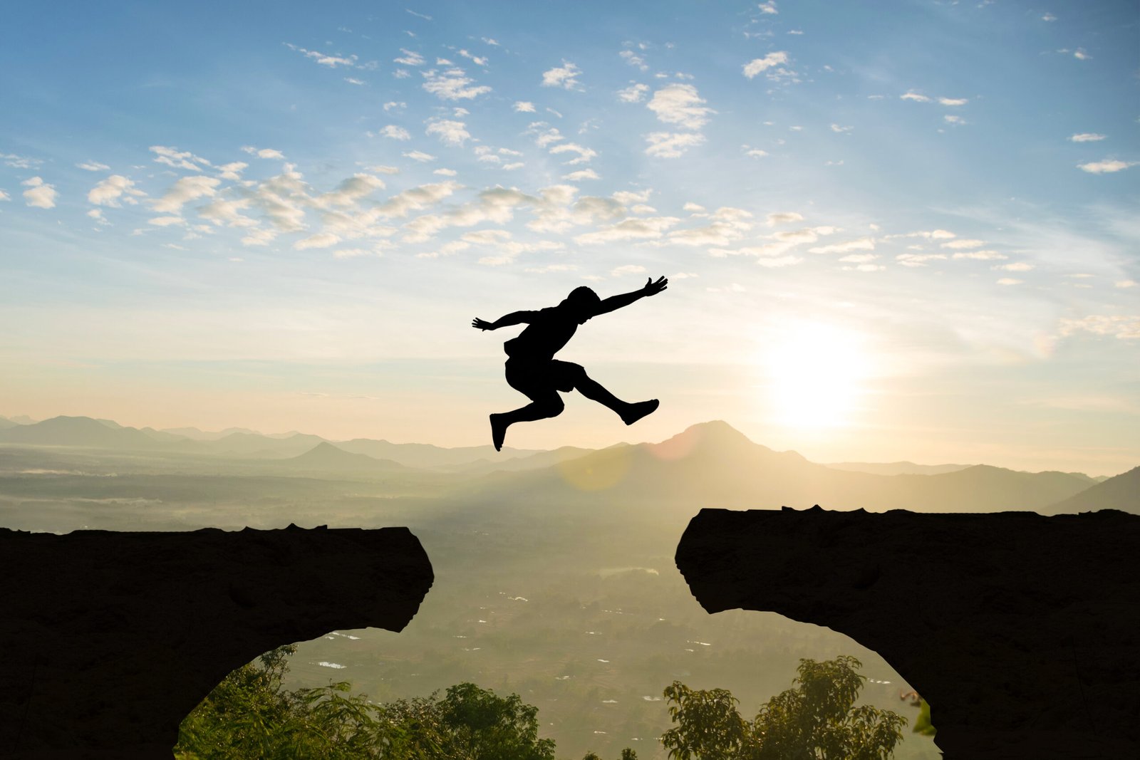 Man jump Mountain cliff sun light over silhouette