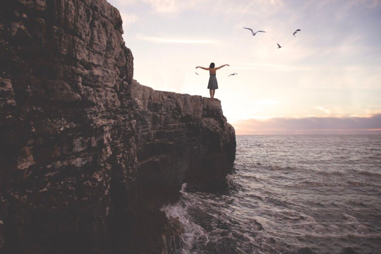 surreal woman with arms outstretched above a cliff in front of a spectacular landscape