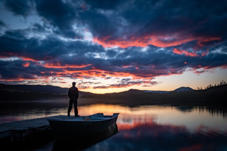 Standing silhouette watching the sunset at the horizon and its reflection over the lake