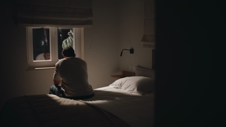 Silhouette sad man sitting bed home looking window feeling lonely. Guy insomnia