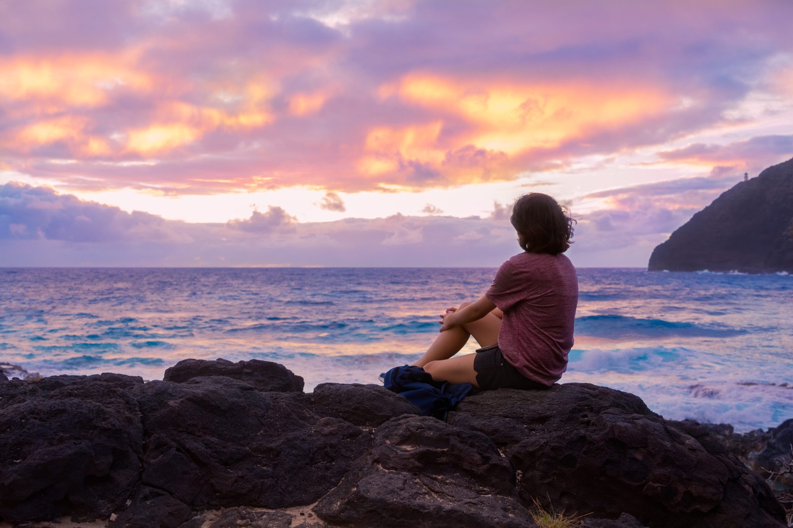 Teen girl sitting on rocky beach watching the hawaiian sunrise