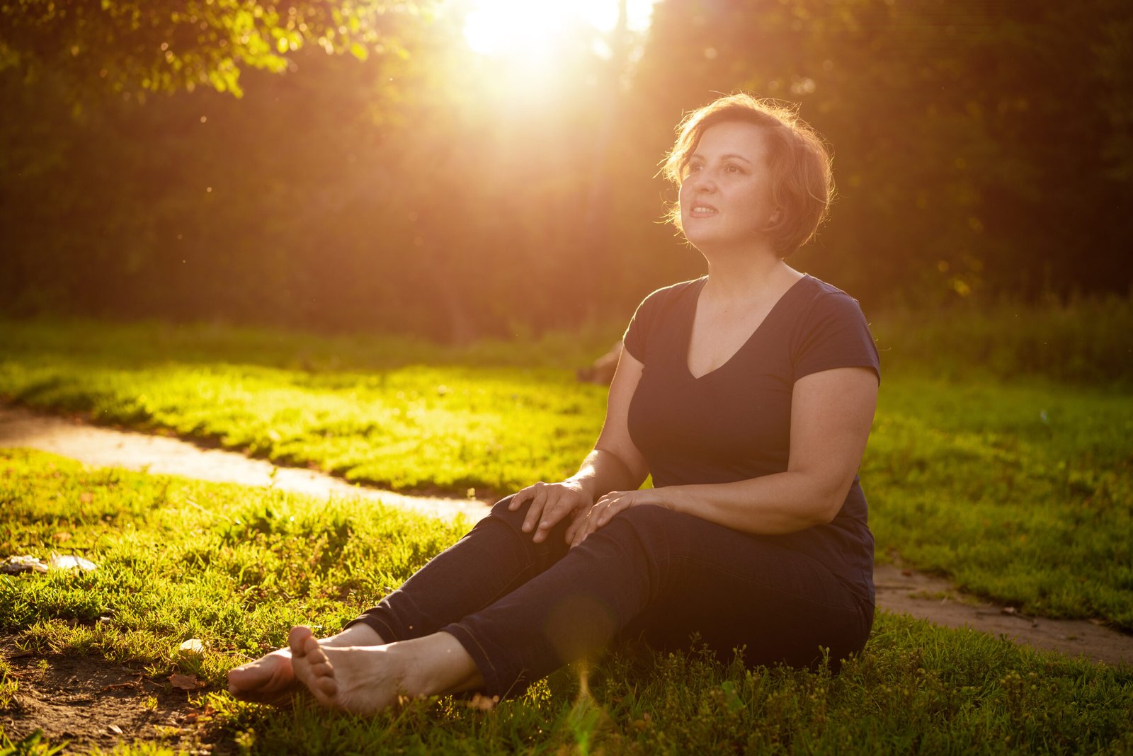 Adult woman sitting in the park on the grass in the rays of sunset Sunny
