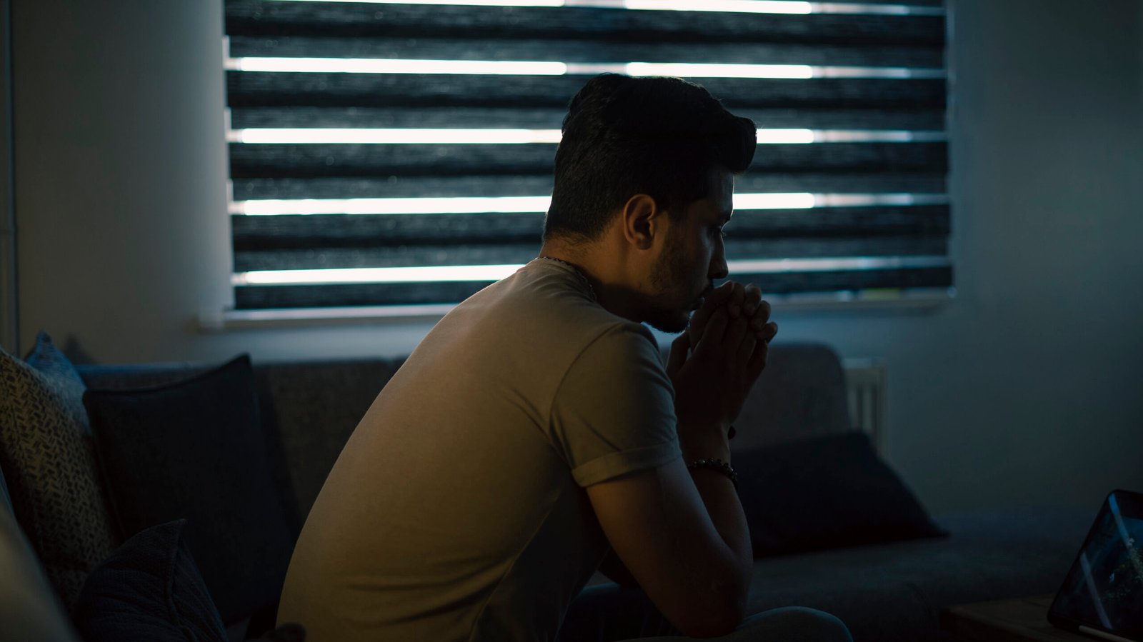 Thoughtful young man in low light. Dramatic concept , man sitting on sofa