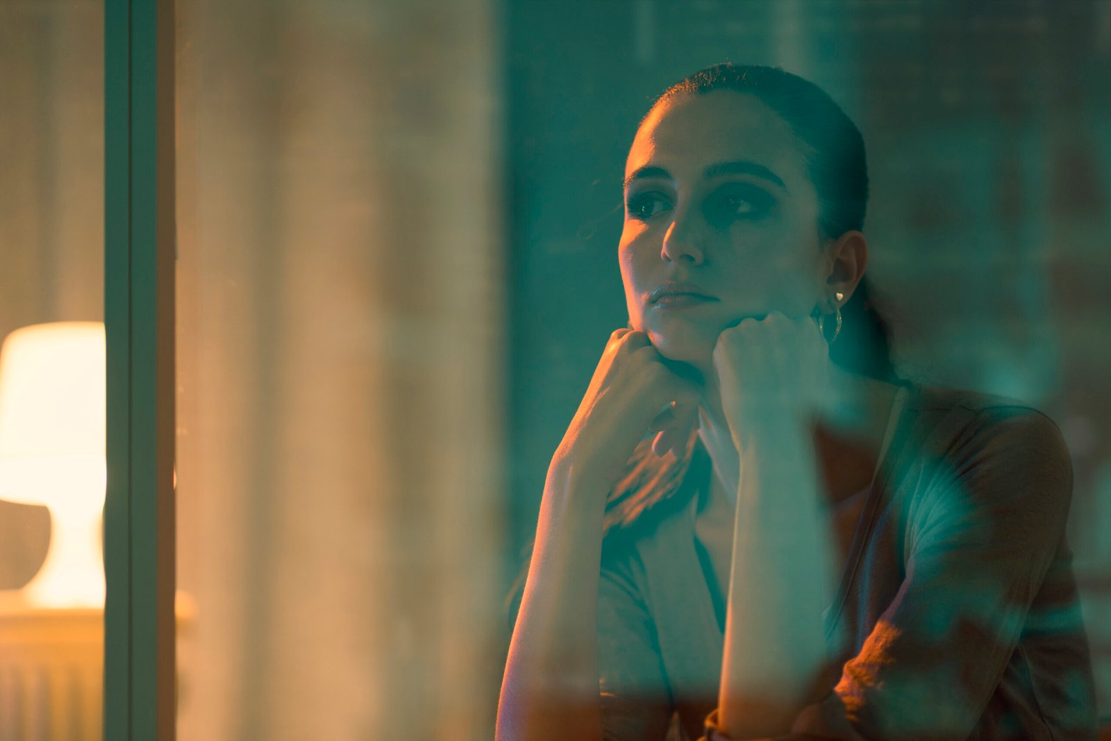 Sad beautiful woman sitting next to a window, she is looking away and thinking
