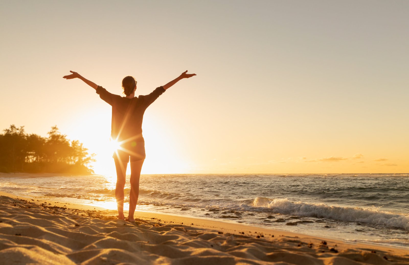 Female with arms up feeling free and energetic on the beach at sunset.