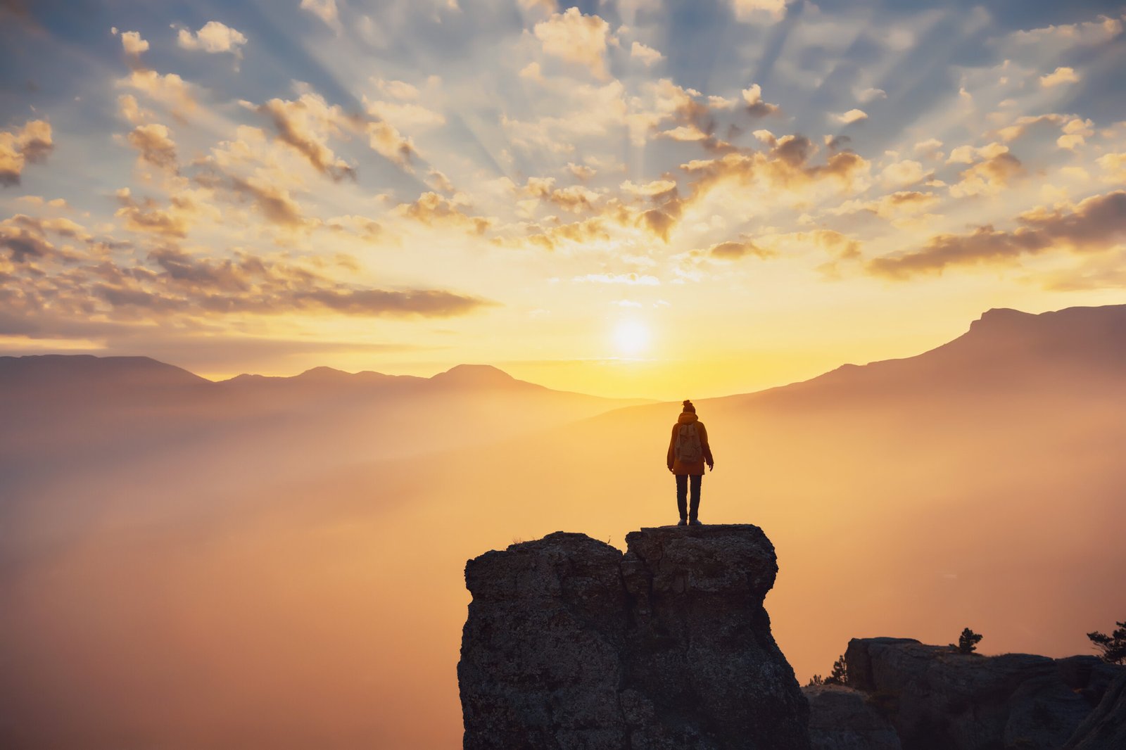 Silhouette of hiker girl enjoying sunlight in mountains at sunset