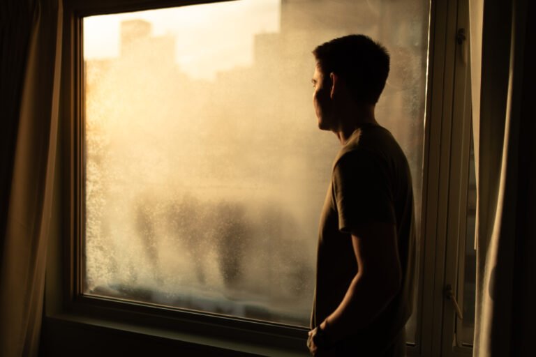 Thoughtful man in city apartment looking out his window.