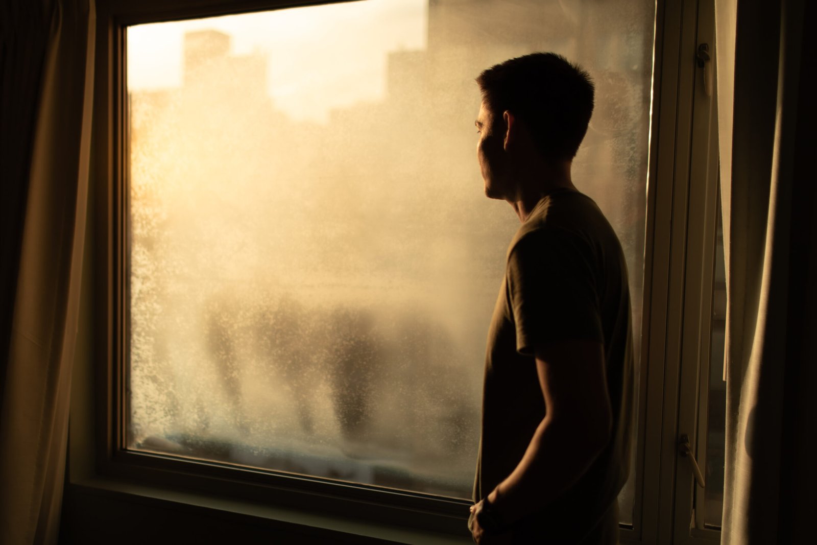 Thoughtful man in city apartment looking out his window.