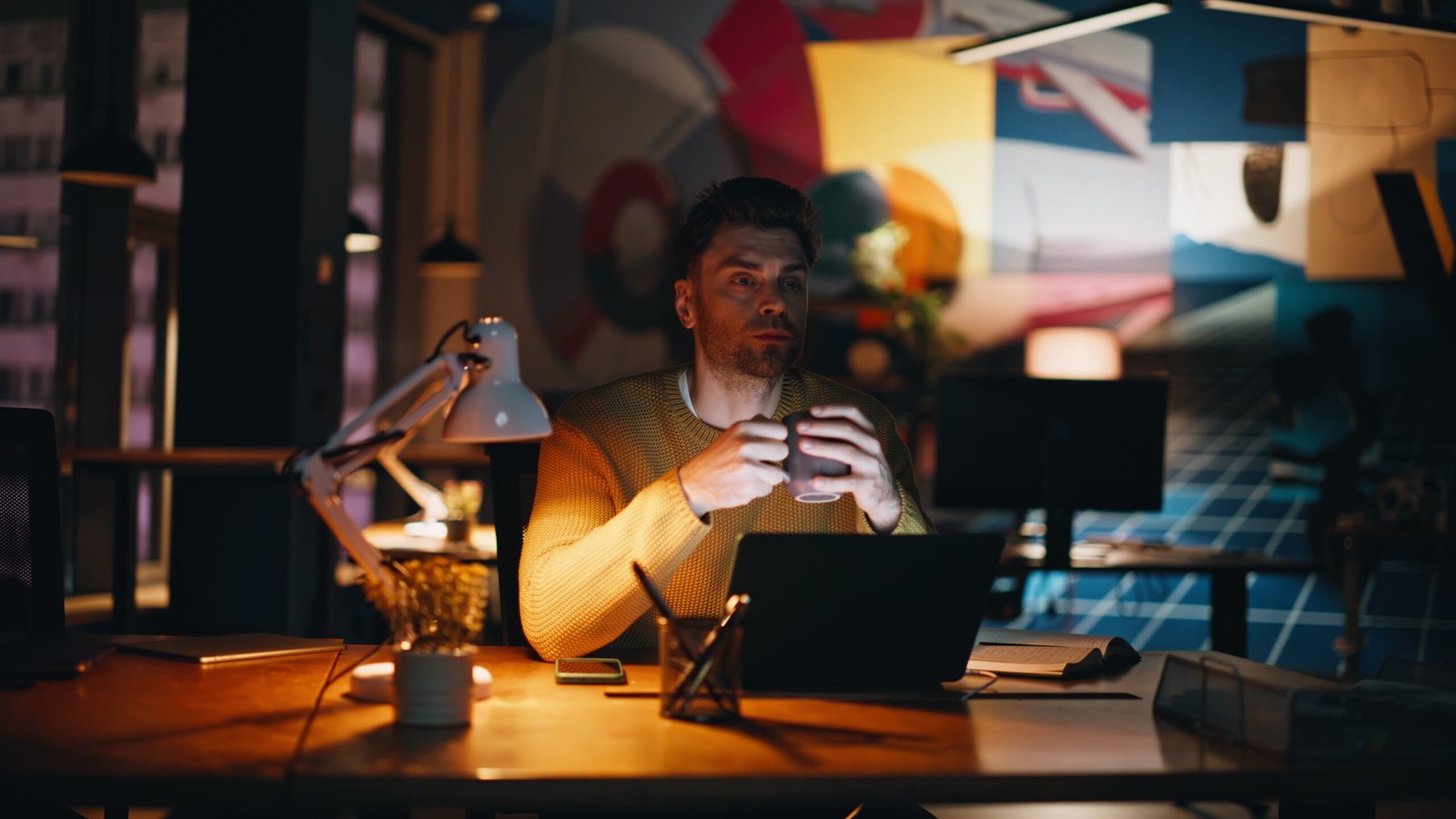 Thoughtful freelancer holding coffee cup sitting at dark office laptop closeup.