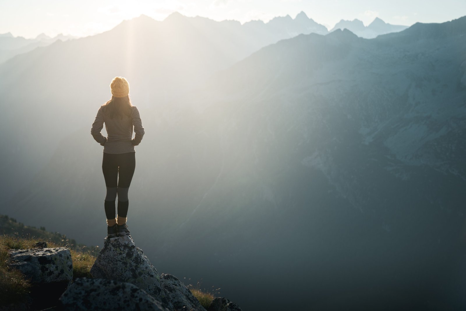 Young Woman Hiker Standing On The Edge Of Cliff At Sunrise. Backlight Sunlight Sunbeam. Copy Space