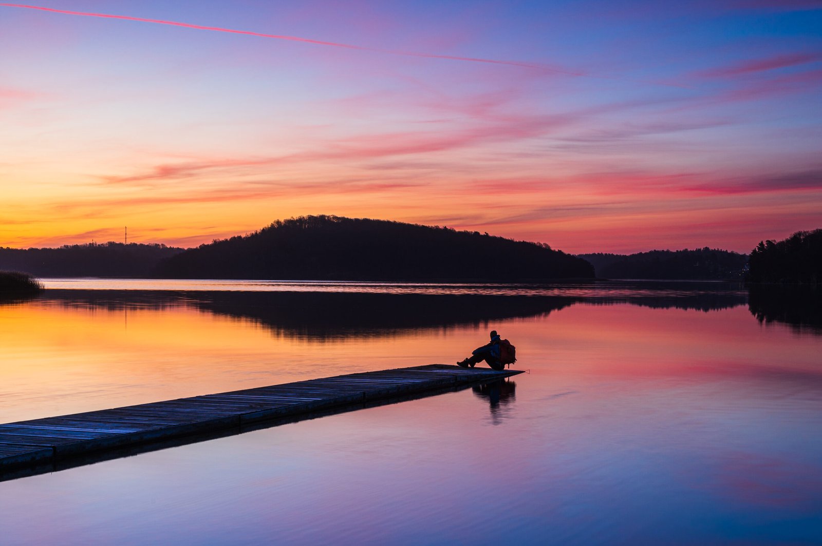 Man sitting on jetty at sunrise
