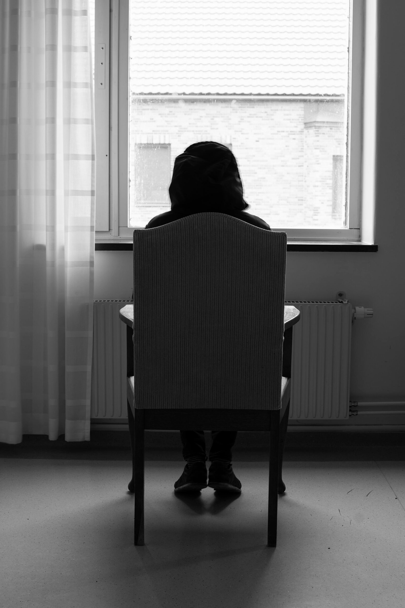 Rear view of depressed person sitting in front of window