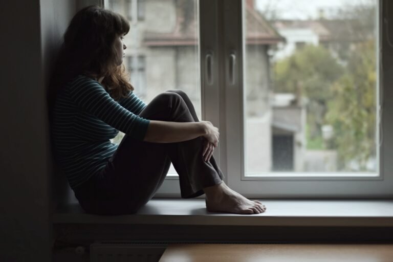 Sad young woman sitting on the window, watching out