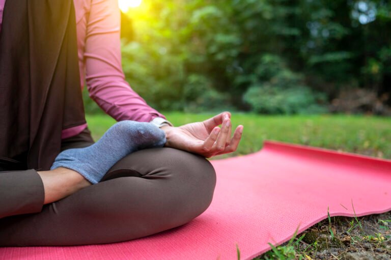 Woman in a sporty outfit is relaxing and meditating zen-like on a fitness mat in a public park outdoors. Concept of a Healthy active lifestyle