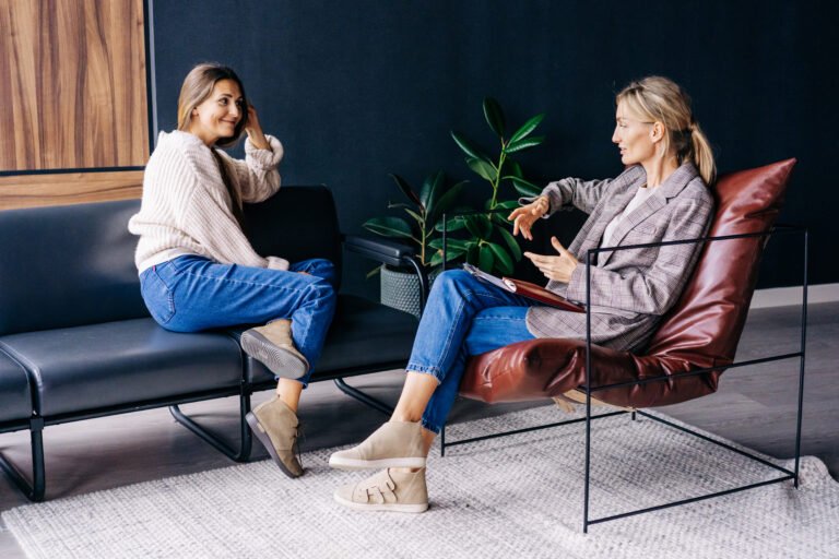 A smiling woman listens to the advice of a consultant psychologist sitting on a sofa in the workshop