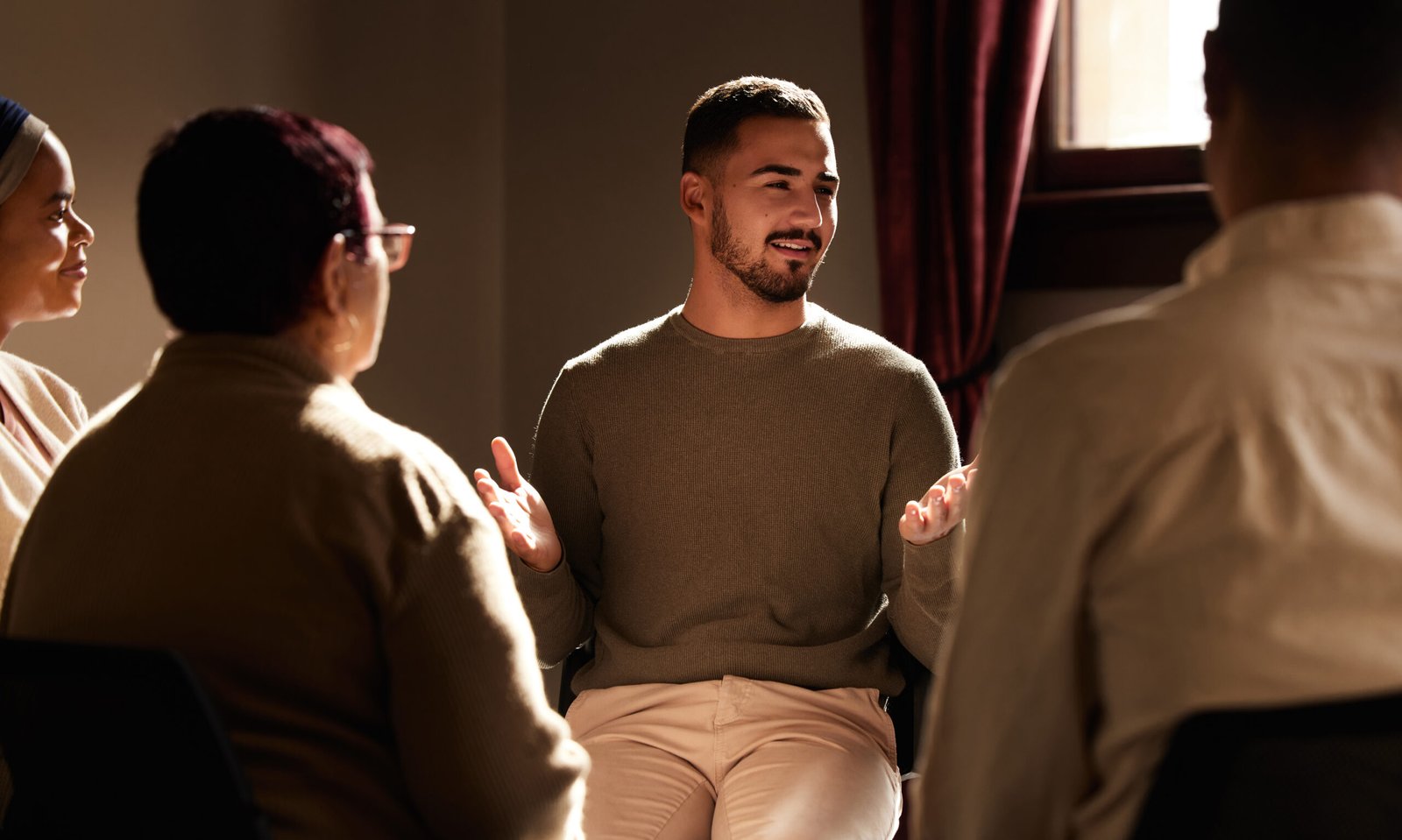 Support, smile and man sharing in group therapy with understanding, feelings and talking in session. Mental health, addiction or depression, men and women with therapist sitting together for healing.