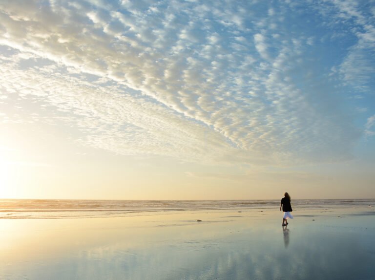 Woman walking on the beach at sunrise.