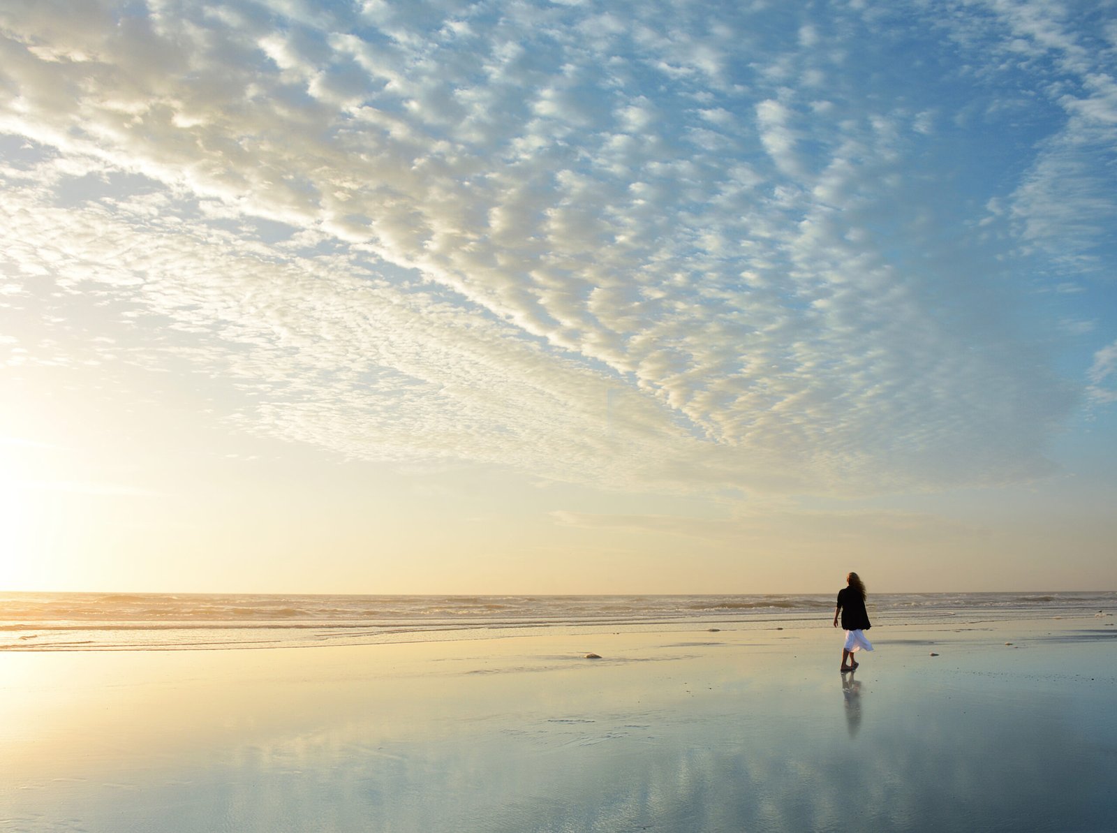 Woman walking on the beach at sunrise.
