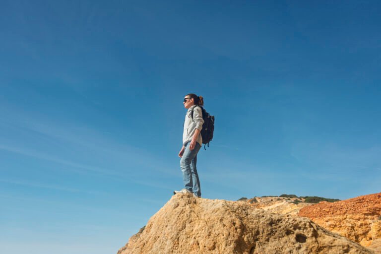 Female Hiker Standing on Cliff Edge Enjoying Scenic Views Under Clear Blue Sky