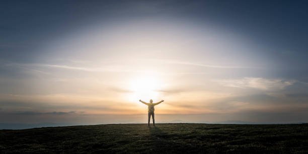Man with arms up standing on top of the mountain at sunset