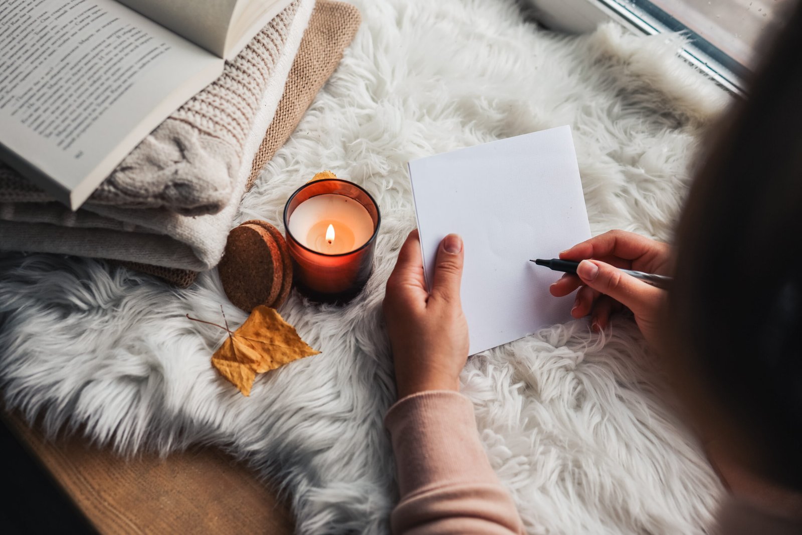 The girl writes a letter on the background of a candle. Home comfort.