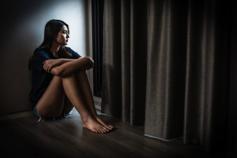 young woman sitting alone in dimly lit room, reflecting on her thoughts. atmosphere conveys sense of solitude and introspection
