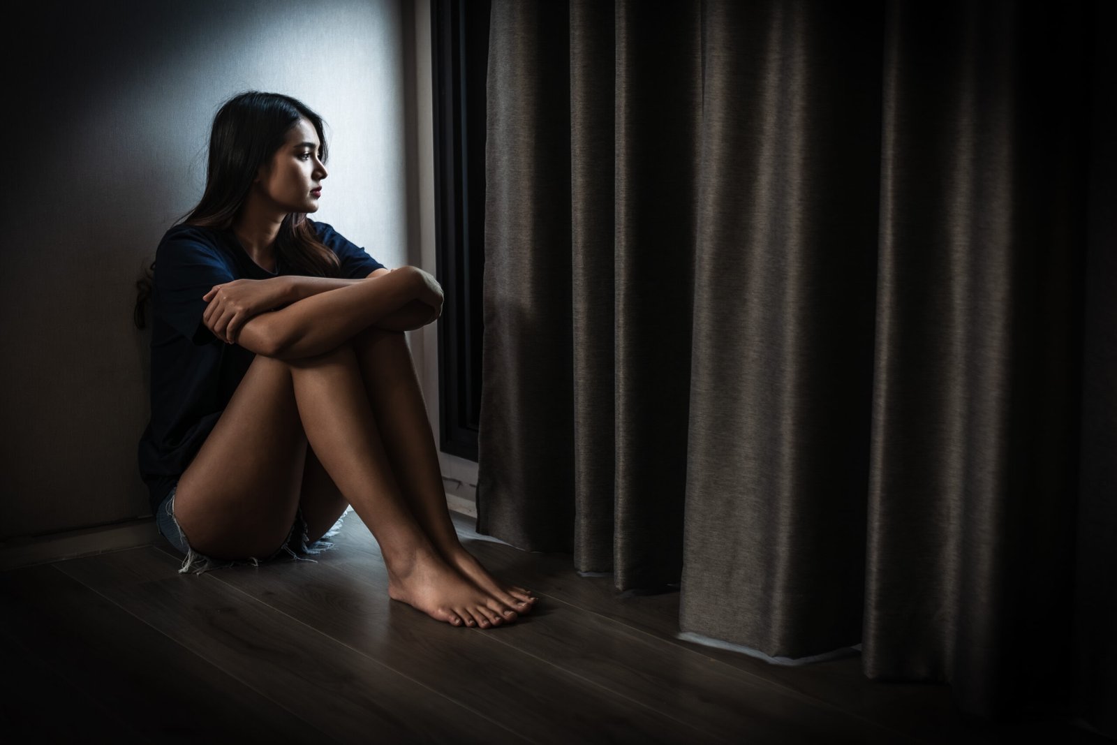 young woman sitting alone in dimly lit room, reflecting on her thoughts. atmosphere conveys sense of solitude and introspection