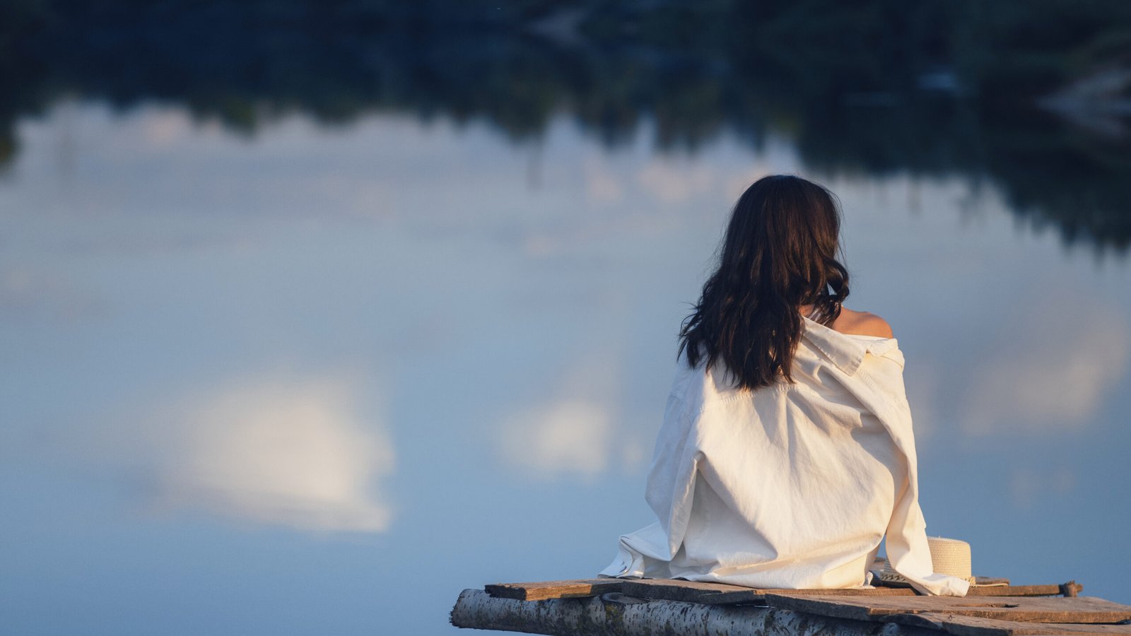 back view of a young woman sitting alone above the water on a bridge.