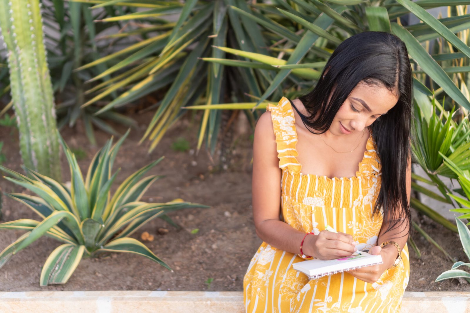 Young latin woman writing in her notebook in a tropical garden