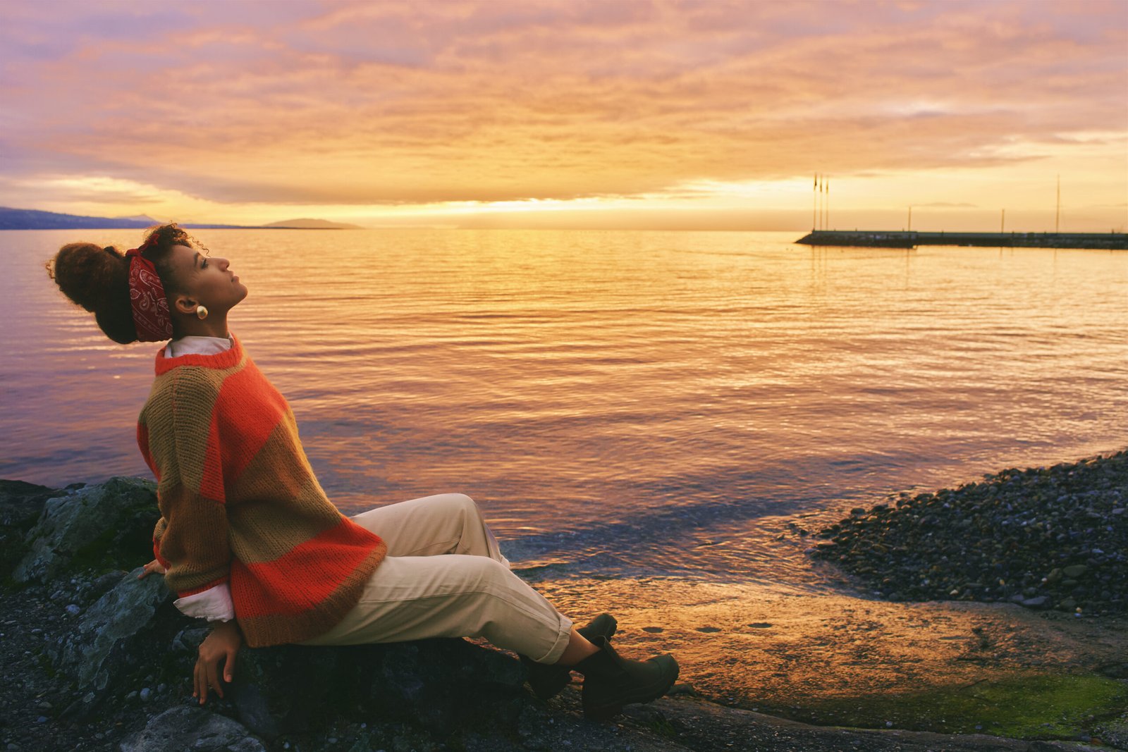 Outdoor portrait of young african woman admiring amazing sunset by the lake
