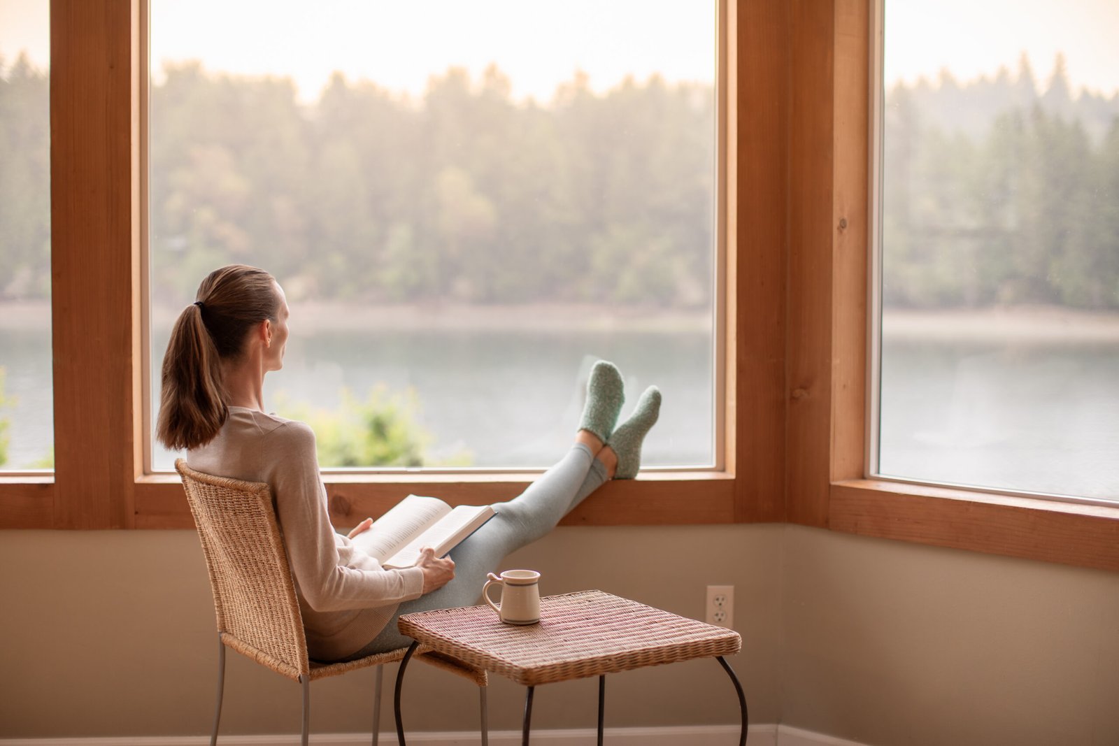 Woman enjoying beautiful view, cup of tea and book at home.
