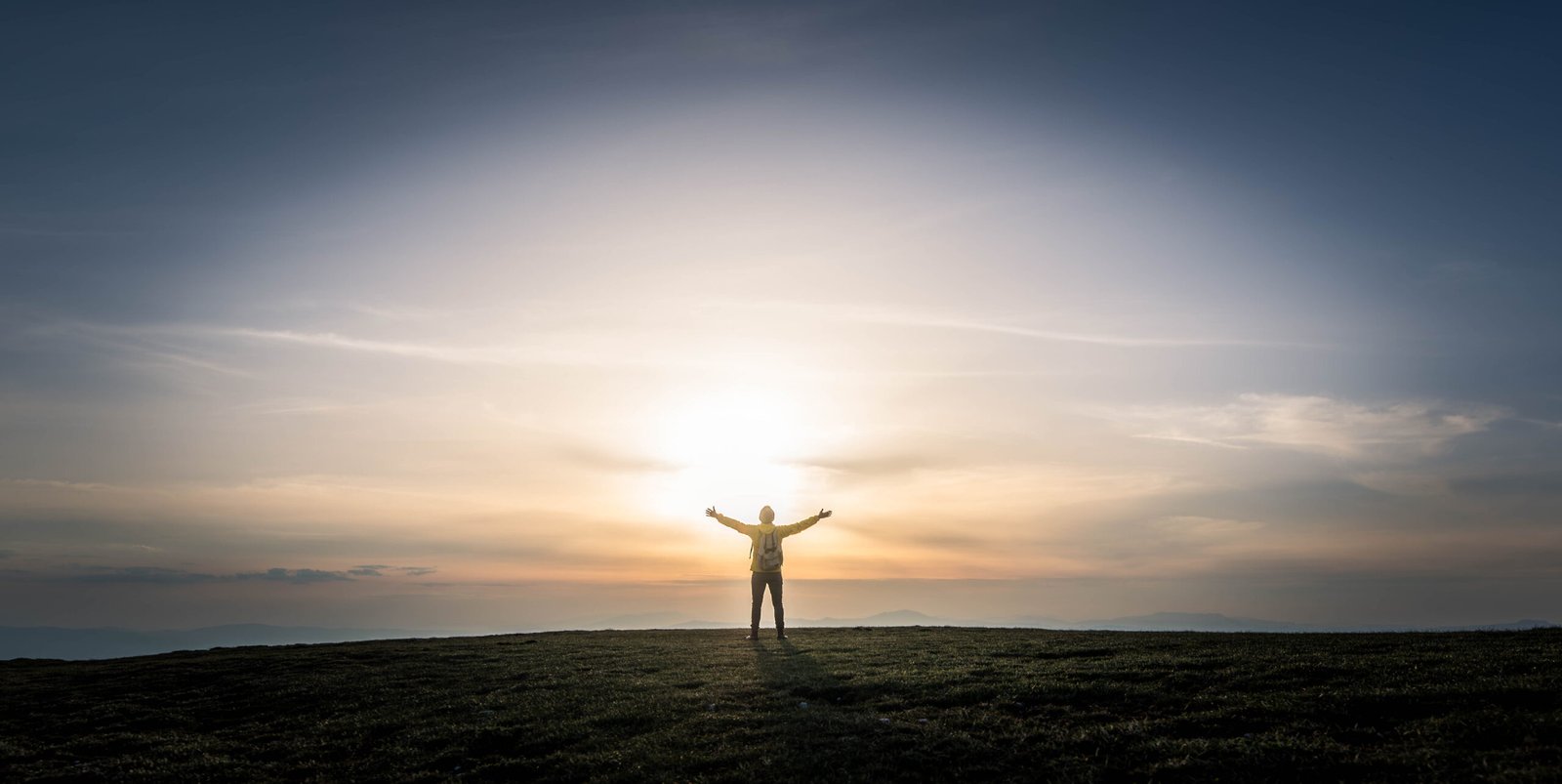 Man with arms up standing on top of the mountain at sunset