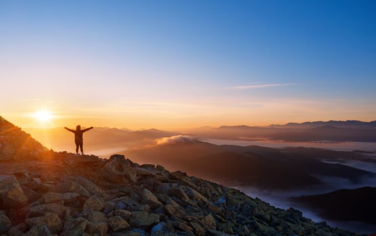 Girl on a mountain top with outstretched arms. Dramatic landscape of a lone hiker looking at mountains in fog at sunrise.