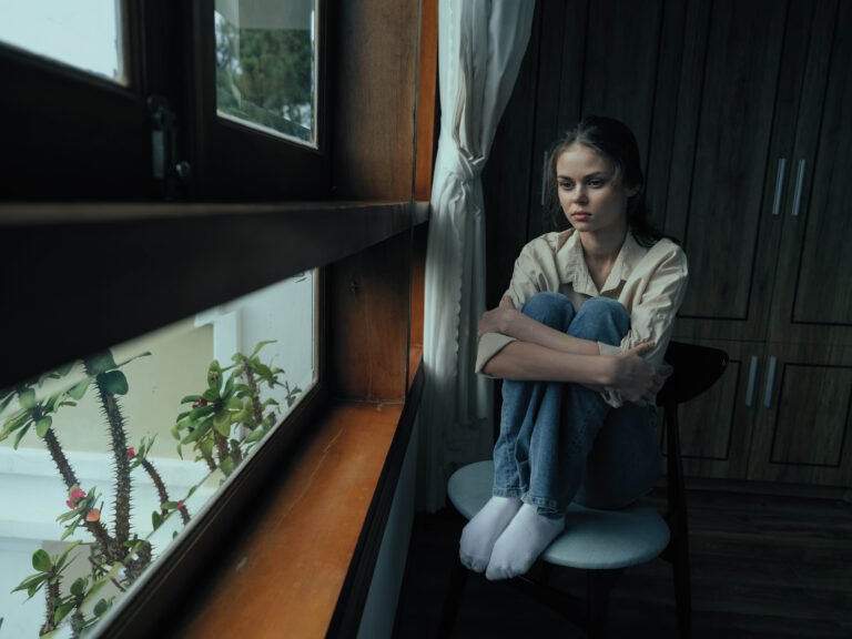 Woman fall depression sitting by the window and looking at nature, rainy weather and discouragement, home life style, loneliness.