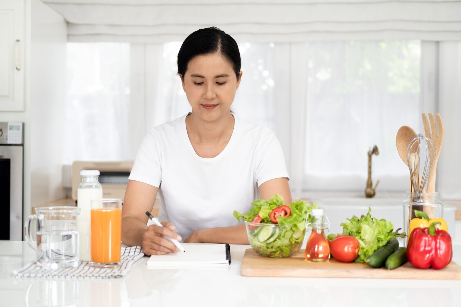 Diet, Dieting asian woman write diet plan right nutrition on table with fresh vegetables salad, is different food ingredients in the green. Nutritionist of healthy, nutrition of weight loss.