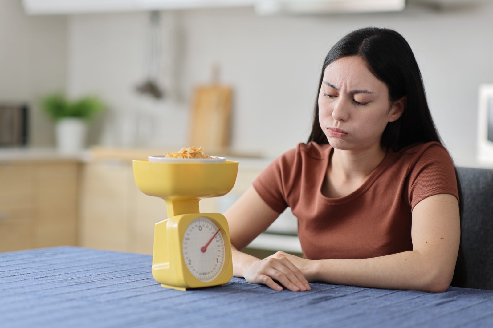 Stressed asian woman weighing food in rthe kitchen