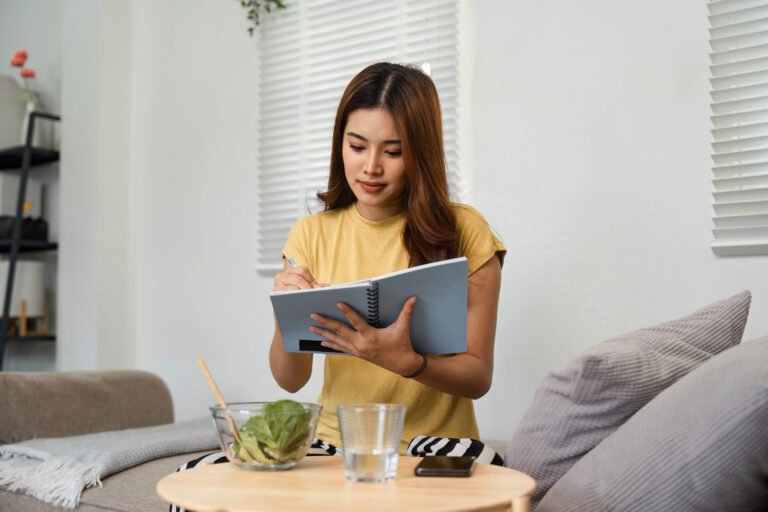 Healthy Living and Mindful Eating. A woman takes notes while enjoying a healthy salad at home.