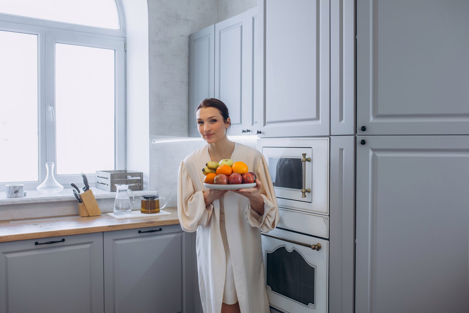 A beautiful brunette woman in the kitchen with a plate of fruit in her hands