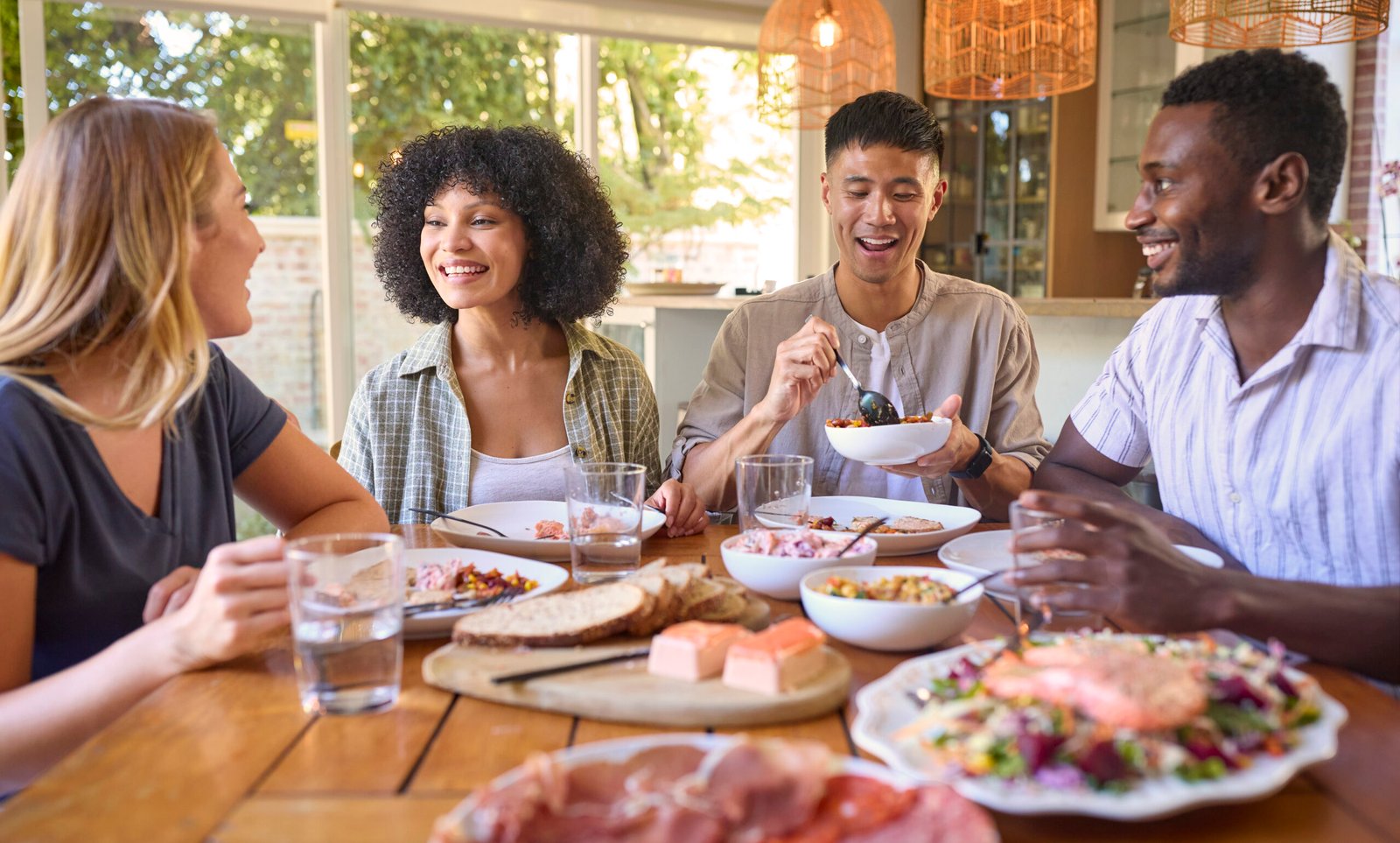 Group Of Multi-Racial Friends Sitting Around Table Enjoying Meal At Home Together