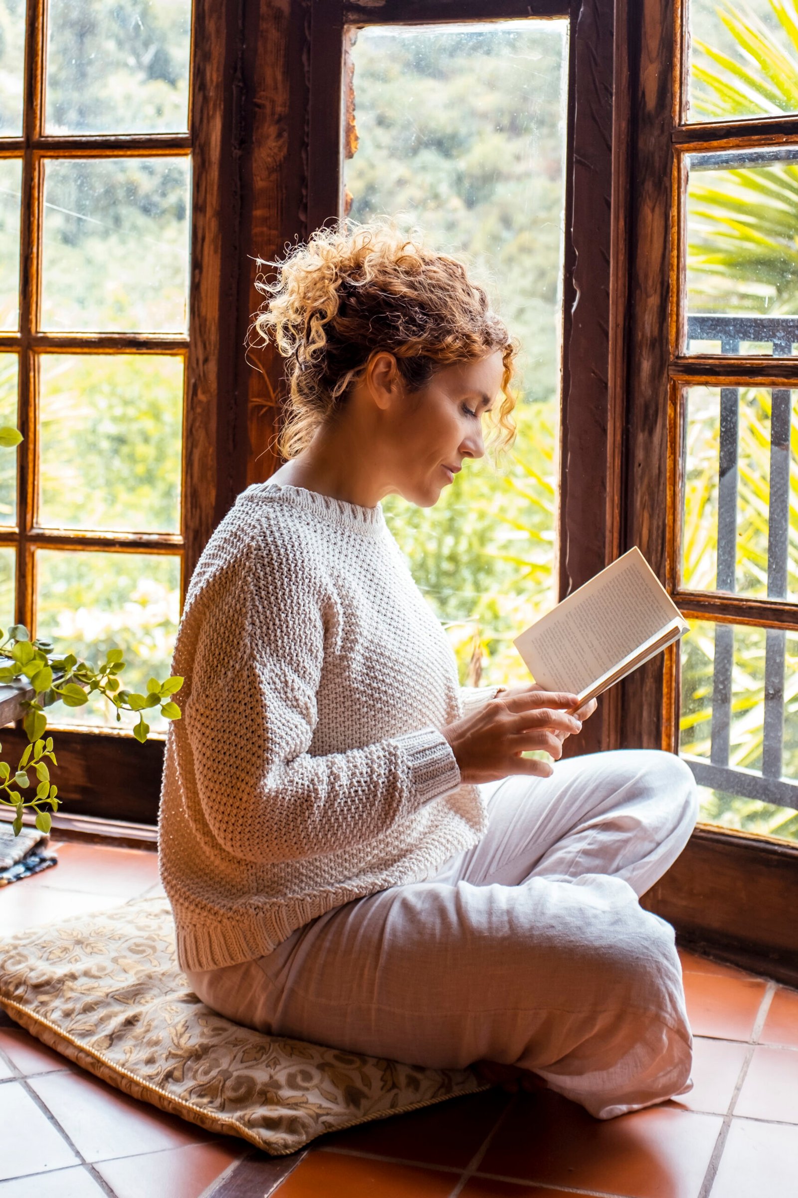 Knowledge for all healthy natural midnful zenlike lifestyle people. One adult woman sitting on the floor at hoe in total relaxation indoor leisure activity alone reading a book. Nature outside view