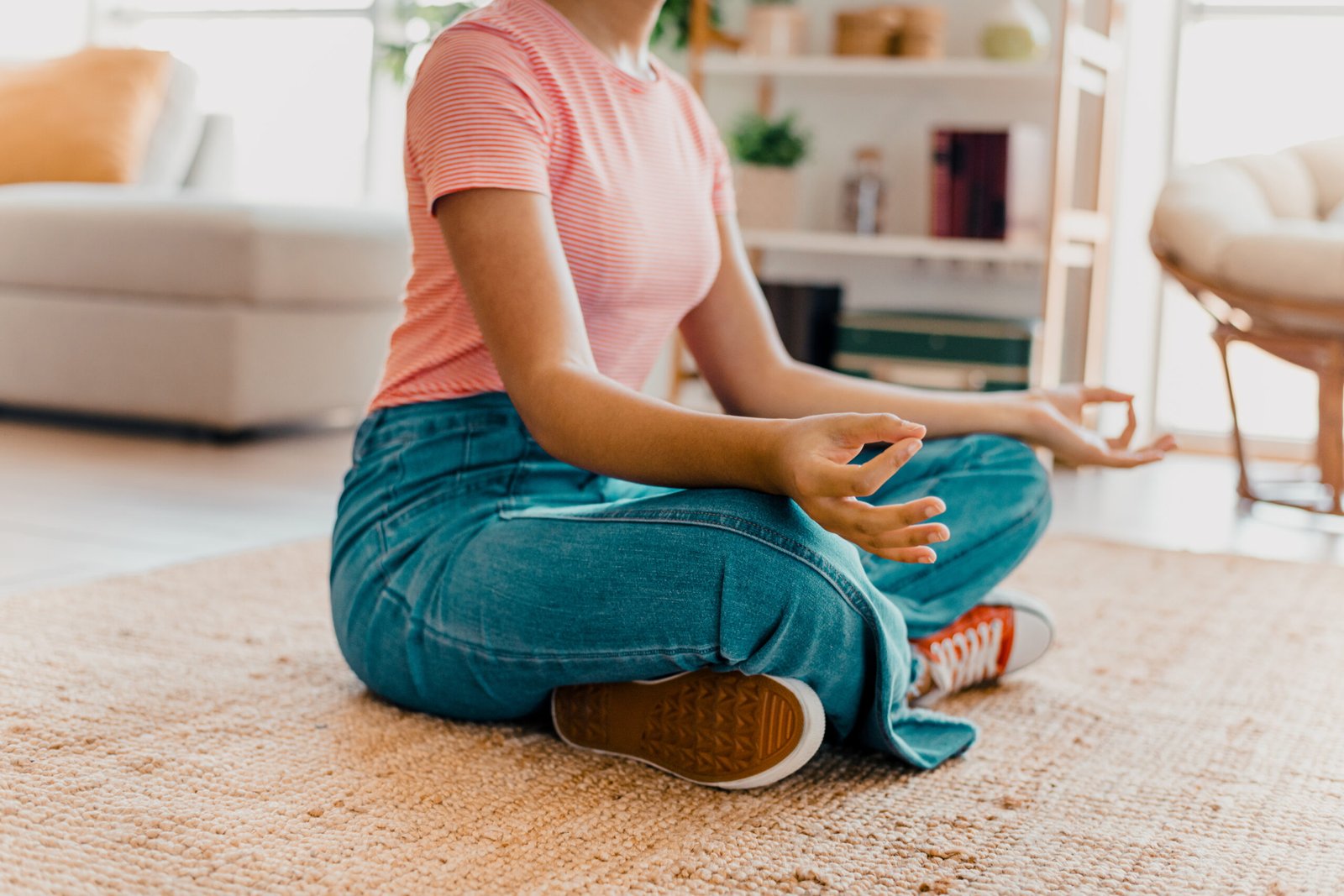 Young woman practicing meditation on a rug in a cozy living room with daylight creating a peaceful and tranquil atmosphere