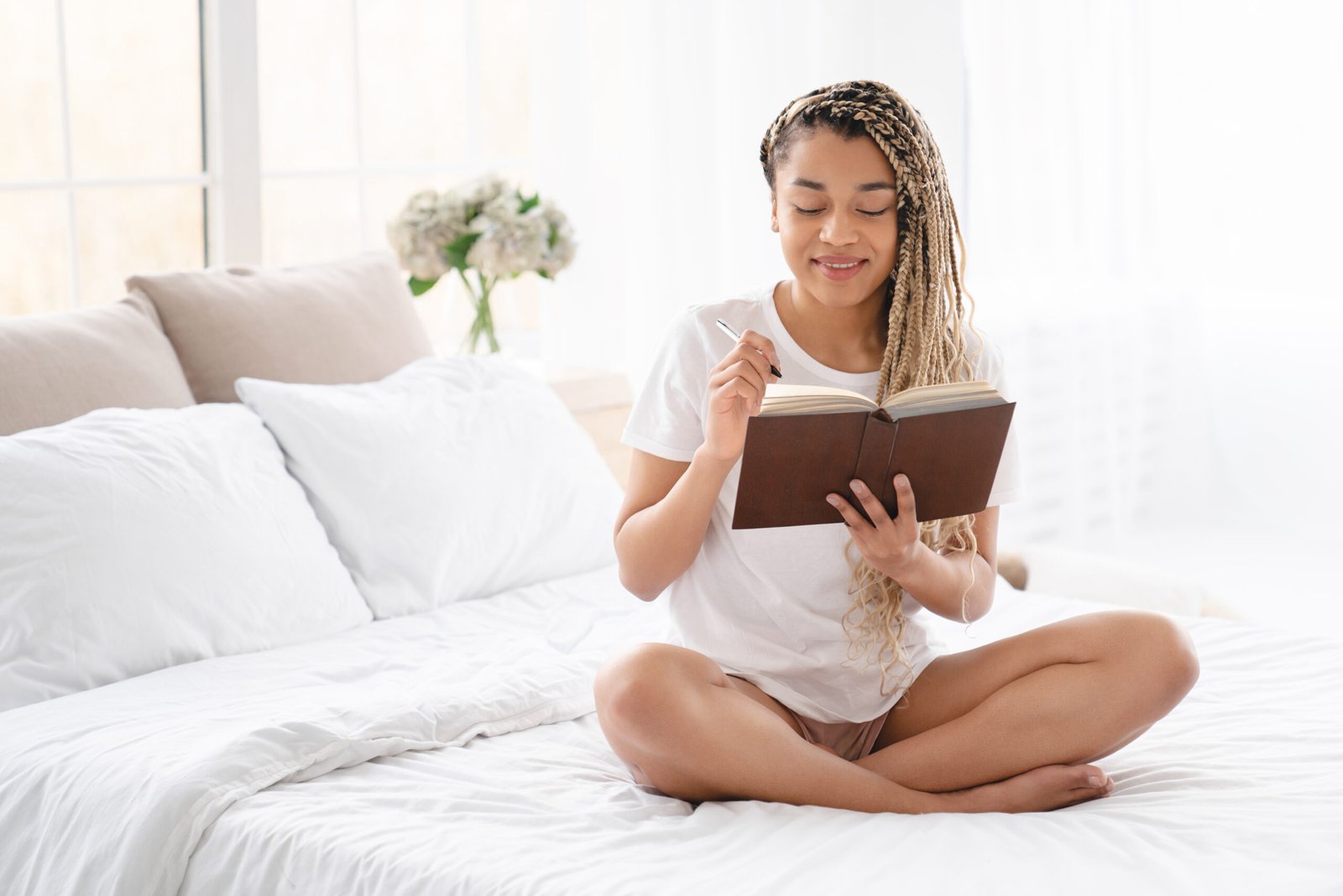 Inspired relaxed concentrated pensive young african-american girl thinking about writing a poem, diary, to-do-list, reading book at home in the bed. New ideas, inspiration.