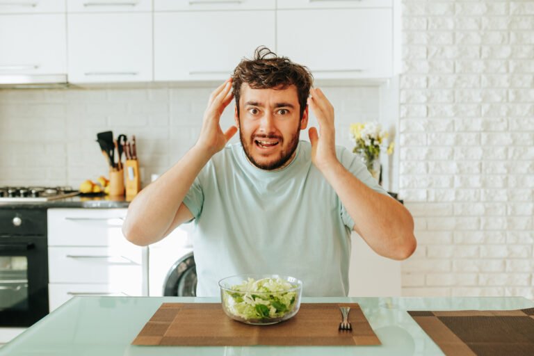 Man shows frustration while preparing to eat a salad in a modern kitchen