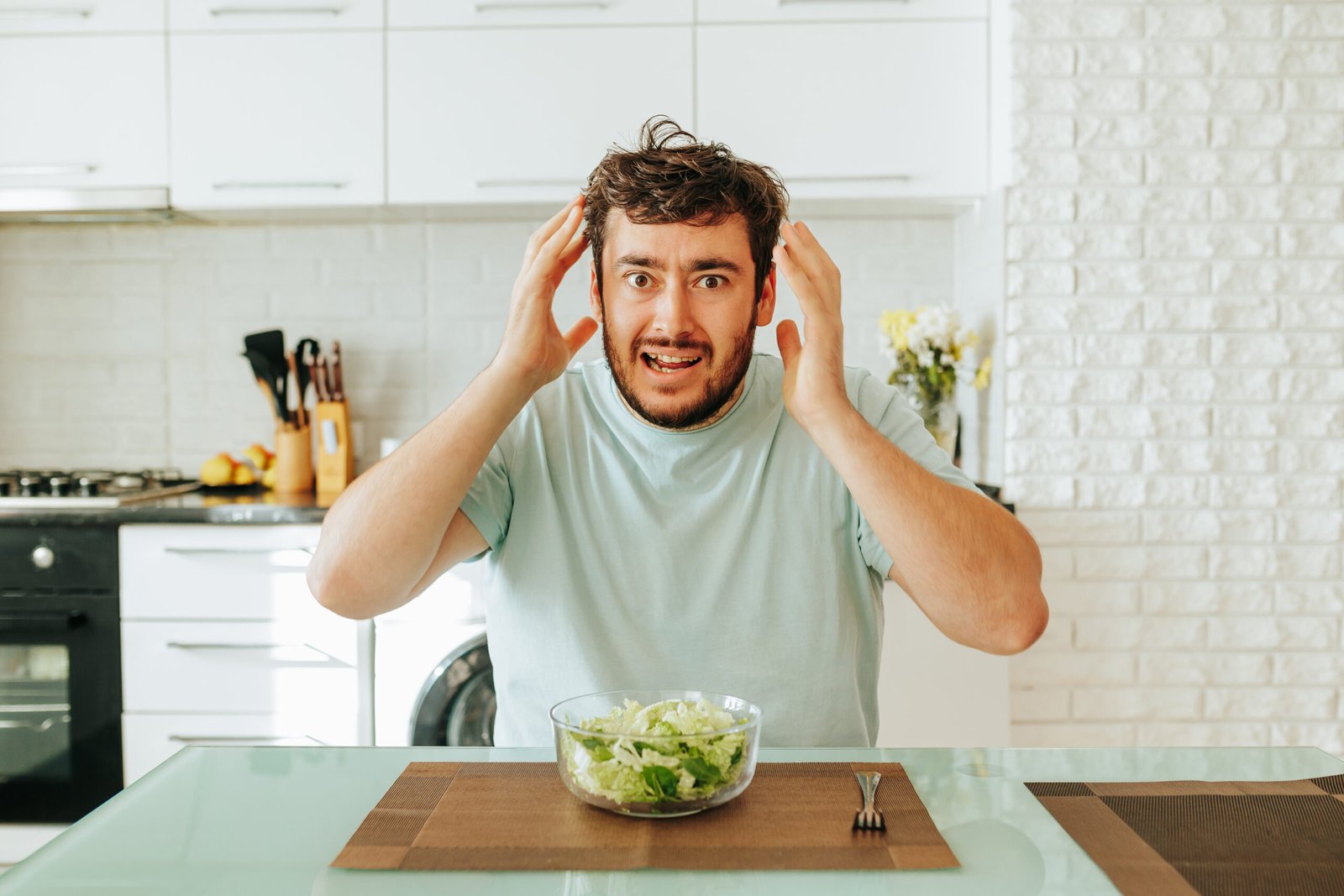Man shows frustration while preparing to eat a salad in a modern kitchen