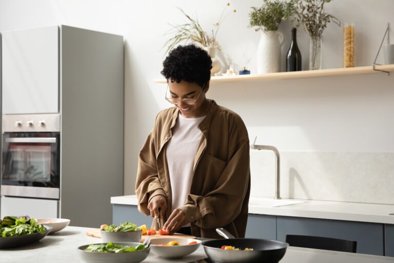Happy young African American woman preparing food in kitchen.