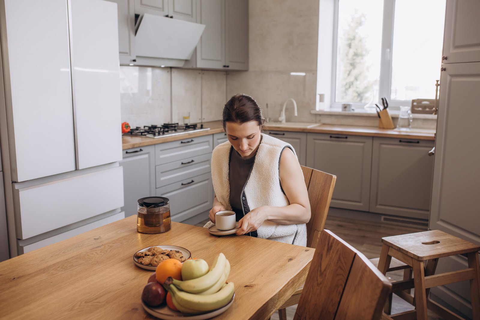 A beautiful brunette woman is having breakfast at the kitchen table with a cup of tea