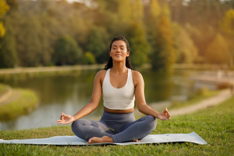 Woman practices yoga sitting in lotus position near lake outdoors