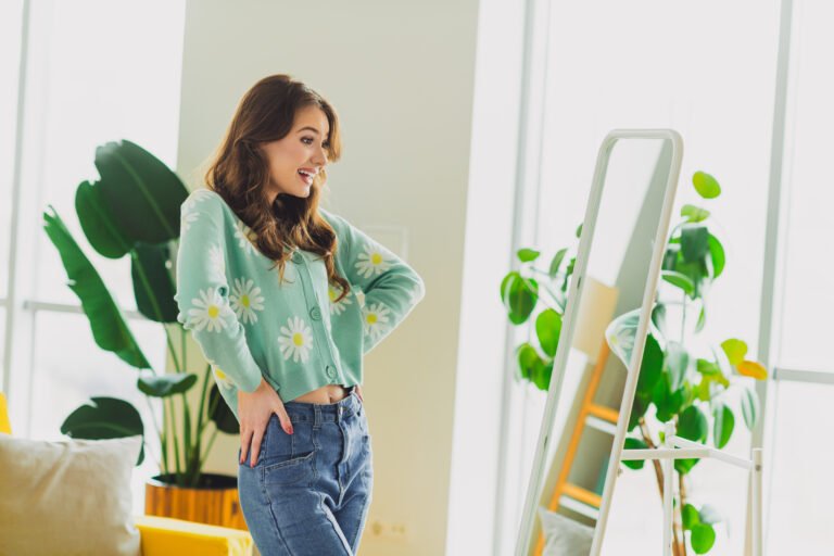 Brunette woman enjoying her reflection in a cozy living room setting with modern decor and a cheerful green cardigan