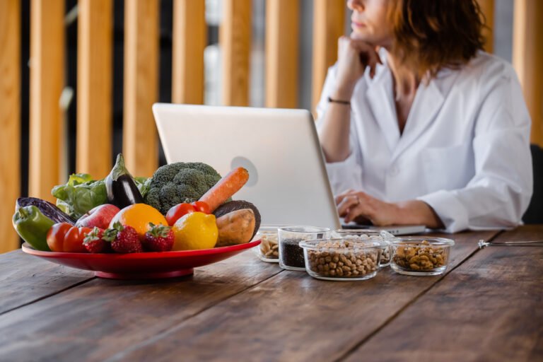 Nutritionist with healthy food typing on laptop in office
